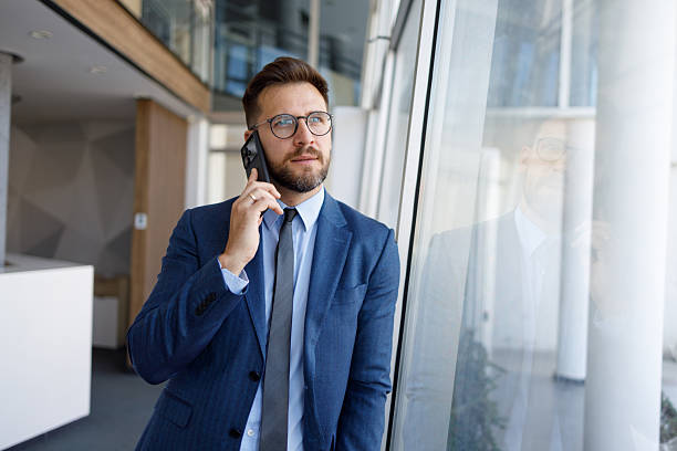 istock Businessman talking on his cell phone while standing near a modern workspace window 2254792169