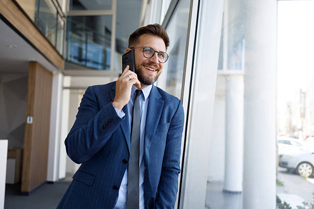 istock Businessman smiling during a mobile phone call in a modern office building, discussing business on a smartphone 2254792220