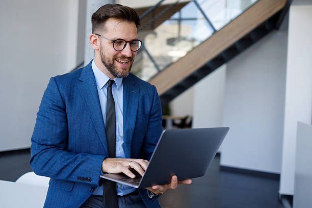 istock Successful businessman in blue suit working on laptop, smiling and checking financial data in a modern office 2254792585