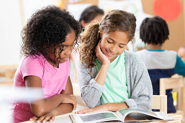 Group of pupils reading books whilst seated at desk smiling to camera