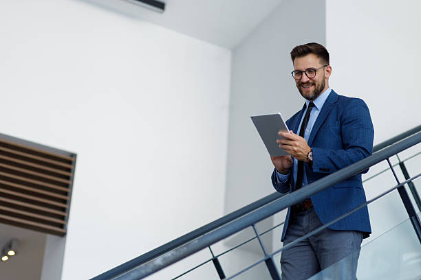 istock Business professional smiling, descending stairs while using a tablet. Concept of mobile technology and corporate communication 2254793357