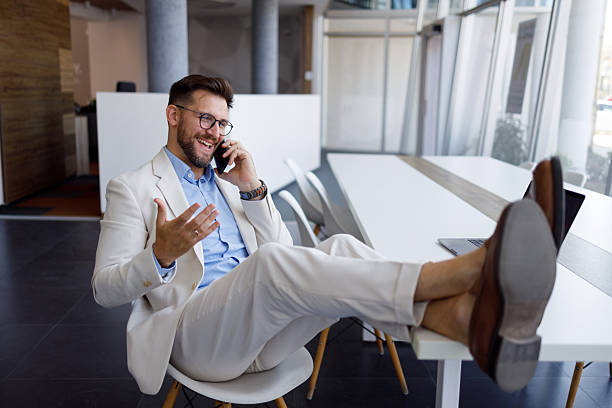 istock Businessman in a suit laughing and talking on his smartphone while relaxing at his modern workplace, showing work-life balance 2254795152