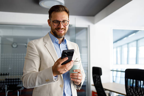 istock Businessman smiling, connecting on smartphone in modern office while holding coffee cup, checking messages or browsing internet 2254795306