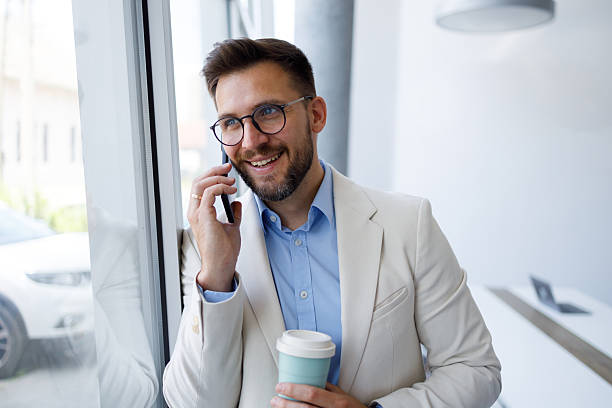 istock Smiling man talking on smartphone, drinking coffee in modern office, staying connected and productive 2254795384
