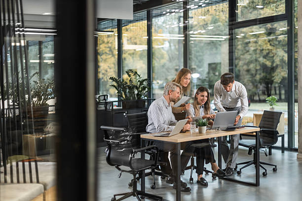 istock Group of business people standing together and discussing their work and projects, having a team meeting in an office, view from glass wall 2254798252