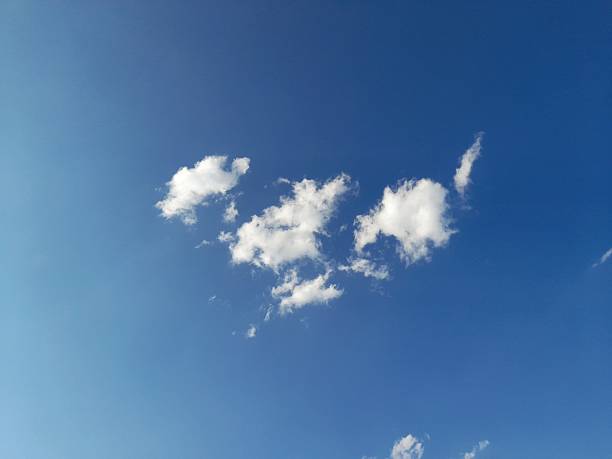 A minimalist low-angle shot of small, isolated cumulus clouds floating in a vast, bright blue summer sky. This high-resolution image features a large amount of natural copy space, making it perfect for background use, inspirational layouts, or weather-related editorial content. The lighting is bright and natural, capturing a peaceful and serene atmosphere.