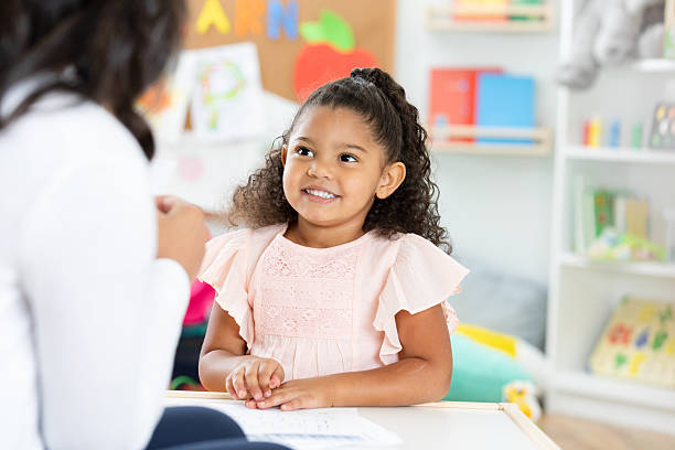 istock Young girl smiling while engaged in an activity with an adult in a classroom setting. 2254803334