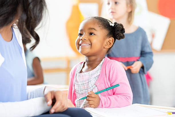 istock Young girl in classroom smiling while holding a green pen, learning and education. 2254803343