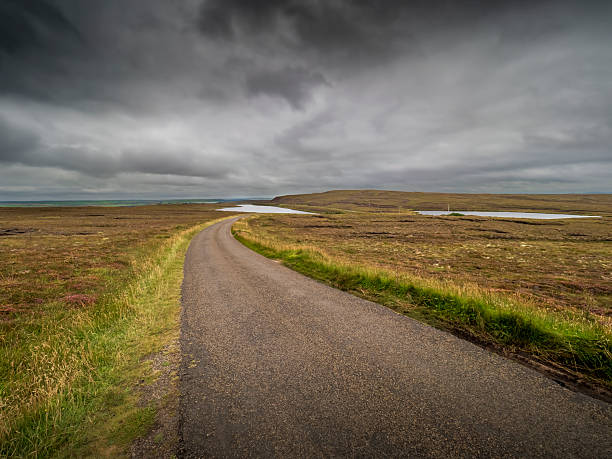 Remote road winding through Scotland's Caithness moorland under a dramatic cloudy sky