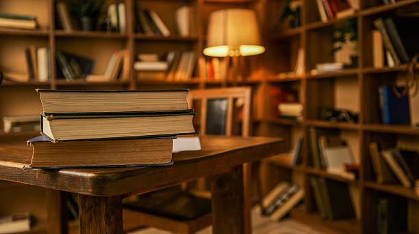 istock Cozy library interior with stacked books on a wooden table and warm lamp light 2254804467