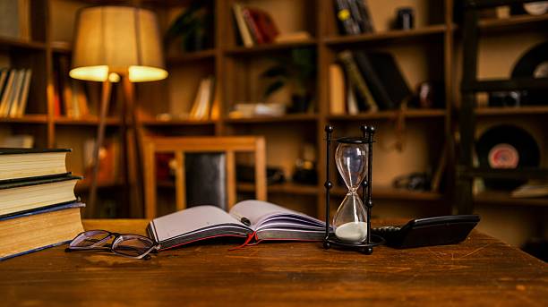 istock Vintage study desk with hourglass, books, glasses, and calculator, evoking timeless learning 2254804472
