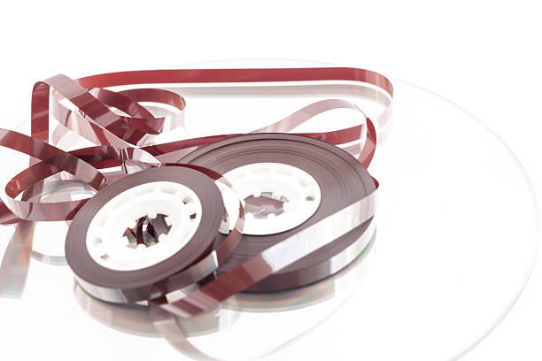 A high-key, clean studio shot of a transparent audio cassette tape laying flat on a pure white surface. The clear plastic casing reveals the intricate internal mechanisms, including the brown magnetic tape, white reels, and copper-colored pressure pad. This isolated object is perfect for graphic designers looking for nostalgic music icons, retro-themed layouts, or concepts related to recording and history.