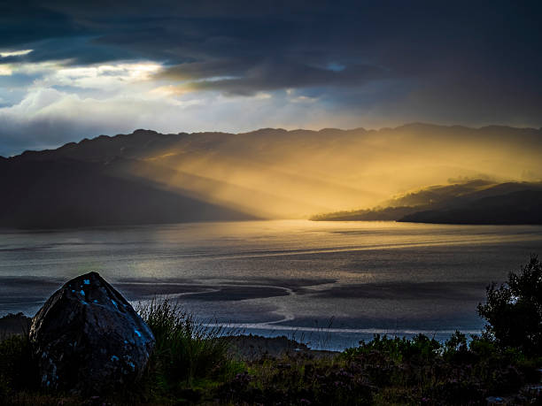 Sunbeams breaking through dark clouds, creating dramatic light on a lake and mountain range