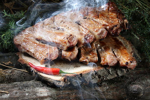 Close-up of a traditional Caucasian dish pork ribs on a grill, cooked over an open fire. Appetizing, juicy ribs are served on a rustic wooden board, garnished with a red chili pepper and fresh herbs. Perfect image for a restaurant menu, culinary blogs, barbecue advertising, or summer picnic.