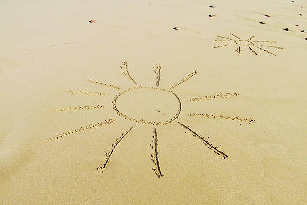 Sun shape drawn on sand with visible texture of grains and smooth lines on a beach surface. Symbolic outdoor scene showing travel concept, romantic gesture, coastal environment, summer setting, creative composition, and nature background