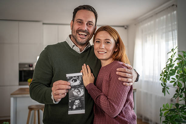 Cheerful heterosexual couple feeling excited about expecting a baby, holding a sonogram image and sharing the news about their future parenthood and family growth
