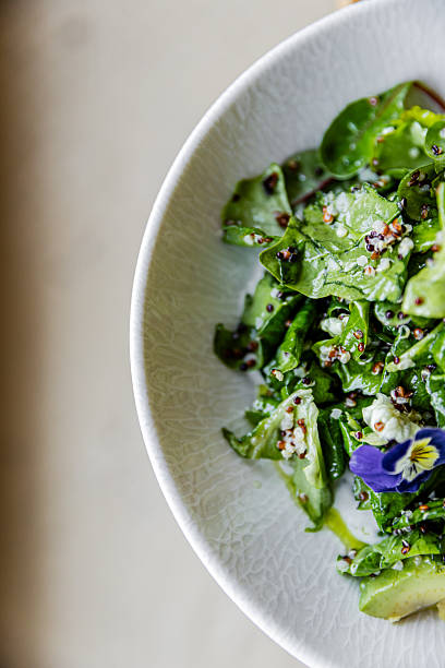 Close-up of fresh green salad with leafy greens, quinoa and edible flower served in white ceramic bowl. Minimal food composition with neutral background and copy space