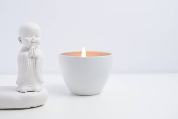 White buddha figurine with burning candle on white background. Zen meditation concept.