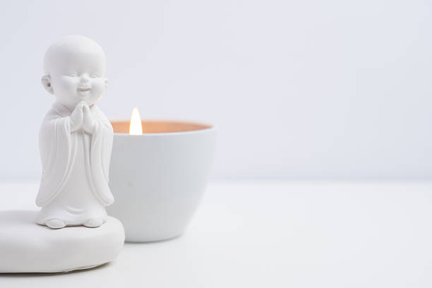 White buddha figurine with burning candle on white background. Zen meditation concept.