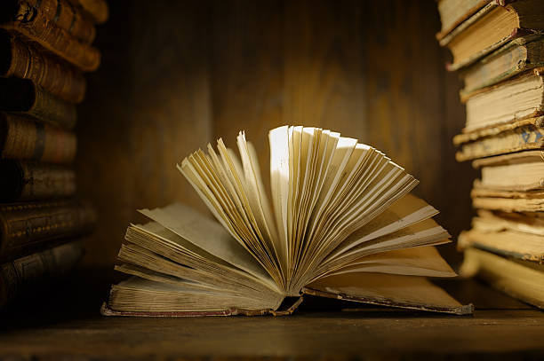 istock An open book rests on a wooden surface surrounded by books.   The setting is a library filled with shelves of books. 2254816924