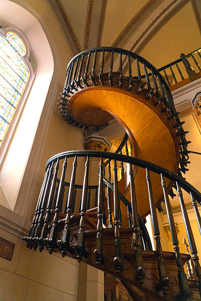 This is a horizontal, color photograph looking down a spiral staircase. The empty stairs in this historic home are carpeted. The railing and wall trim is wooden. Focus is on the end of the railing.