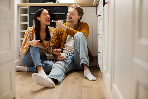istock Happy couple sitting on kitchen floor, man feeding wife with natural yogurt, enjoying romantic atmosphere in relationships 2254820607