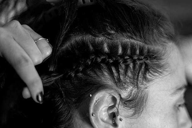 Woman's hand braiding black hair into a cornrow hairstyle with ear piercings visible