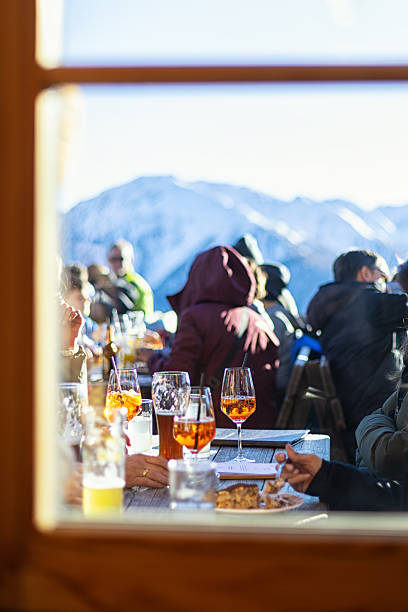 istock Alps lunch, mountain apperitif. Focus is on a glass with a spritz,  a Venetian wine-based cocktail. Defocused people, skiers enjoying lunch in winter mountains. No visible faces. Italy, Tirol, Winter, ski. 2254821883