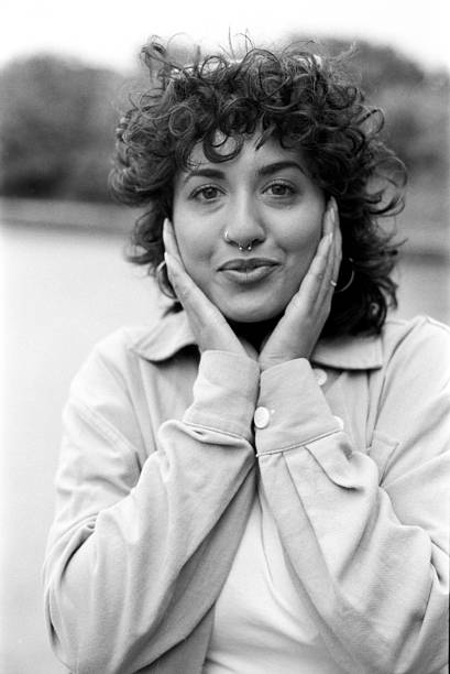 Grainy monochrome portrait of a young woman with curly hair and a nose piercing, holding her face with her hands, conveying a sense of thoughtfulness and introspection