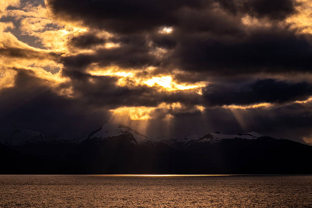 Dramatic sunbeams striking snow-capped mountains on the Alaskan Coast.
