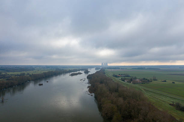 Aerial perspective of the Loire river curving between winter fields and bare trees under a dramatic cloudy sky near Dampierre. The muted light and distant horizon evoke a sense of quiet solitude.