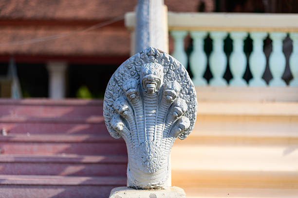 Close-up of a carved stone naga balustrade featuring multiple serpent heads at the Royal Palace in Phnom Penh, Cambodia. The sculptural detail is highlighted by bright daylight, with blurred steps and traditional architecture in the background.