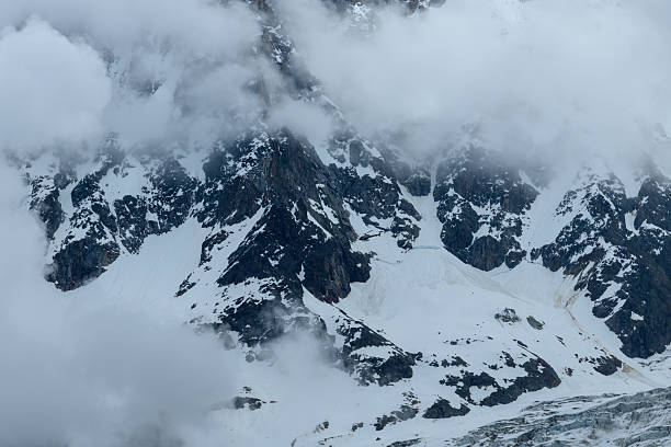 istock Snowy mountain wall shrouded in low clouds 2254843090