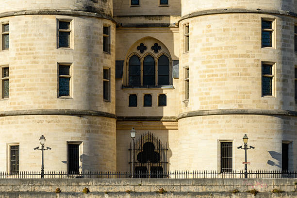 Detailed view of two rounded stone towers with narrow windows and a central Gothic arched window, illuminated by warm sunlight on the facade of La Conciergerie in Paris.