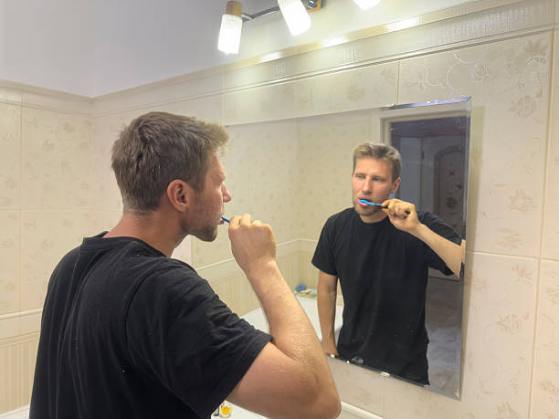 istock A man stands in a bathroom brushing his teeth in front of a mirror 2254846602