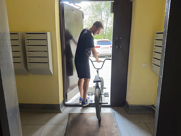 A person is moving a bicycle from outside into a building through the entrance door.