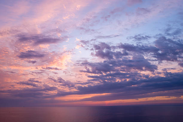Soft lavender and peach clouds drift across a tranquil Mediterranean Sea at sunset, with gentle light reflecting on the water and creating a peaceful, atmospheric mood.