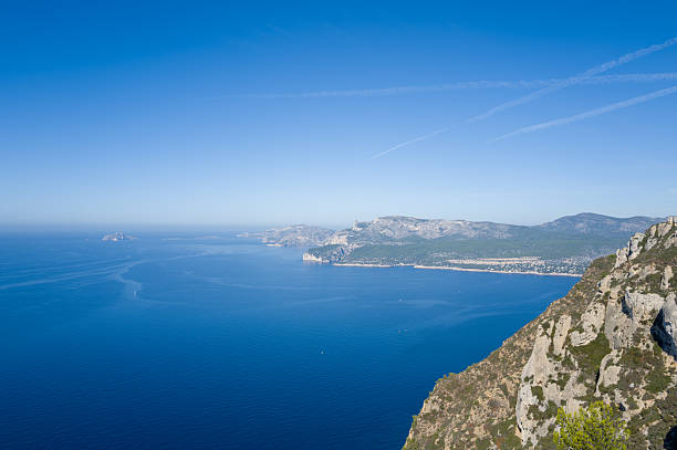 High vantage view over the rugged limestone cliffs and deep azure Mediterranean Sea near Cassis, with distant coastline and mountains under a clear blue sky. The scene conveys vastness, tranquility, and natural beauty.