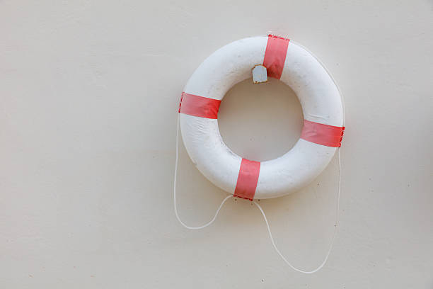 A white and red life preserver is hanging on a wall. The red band is tied to the white ring
