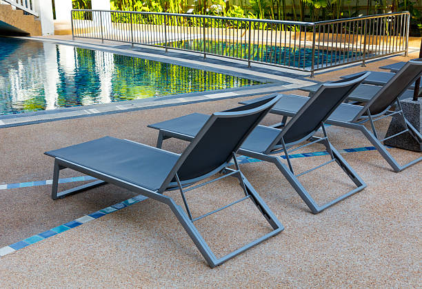 istock Four lounge chairs are sitting on a concrete patio next to a pool 2254856177