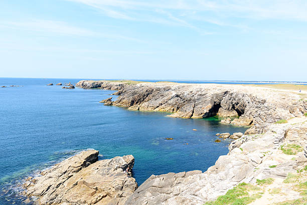 Sun-bleached rocky cliffs frame a tranquil turquoise inlet at Pointe Beg-An-Aud in Saint Pierre Quiberon, with clear blue water and a bright, open sky creating a serene coastal atmosphere.