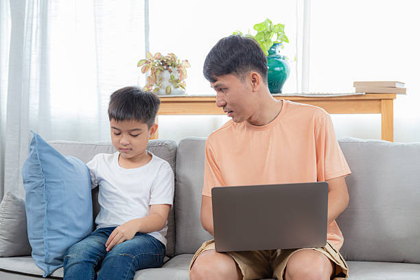 istock Father and son sitting on sofa, engaged in homework. dad tasks help with schoolwork education concepts while working freelance using a laptop. little boy writing on paper, family bonding relationship 2254864049