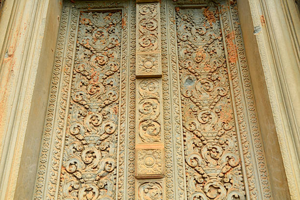 Close-up of ornate sandstone relief with intricate floral and scroll motifs at Baksei Chamkrong temple near Angkor, Cambodia. The weathered surface highlights fine craftsmanship and historic Khmer design under soft daylight.