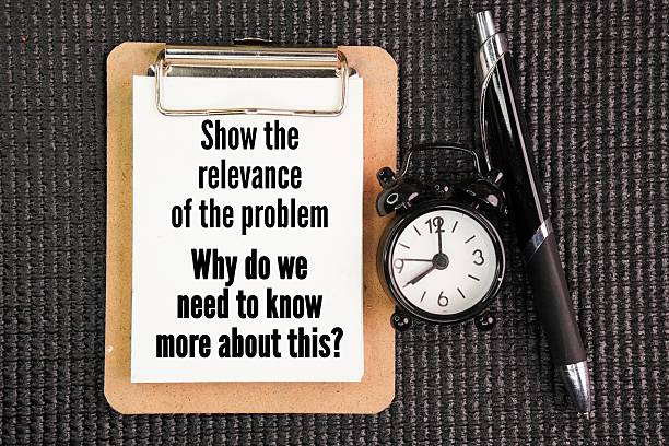 istock Pen, bell clock and paper board write with question words Show the relevance of the problem. Why do we need to know more about this? 2254864283