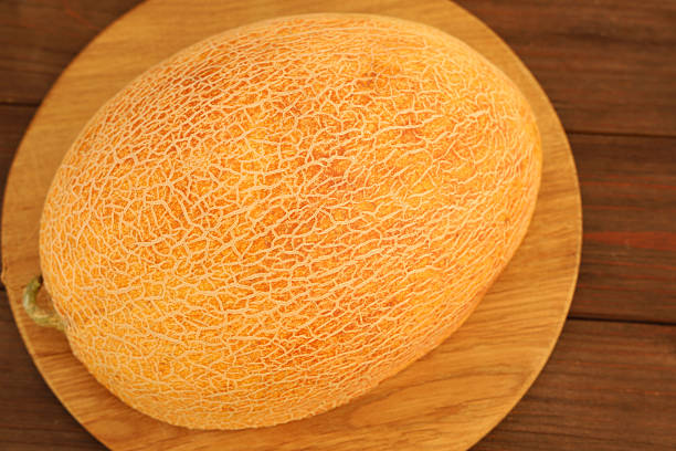 A whole melon rests on a wooden cutting board in a kitchen. Natural light highlights the texture of the melon. The setting is organized focusing on healthy food preparation.