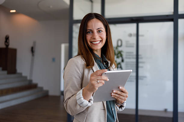 istock Professional businesswoman smiling while holding a digital tablet in modern office environment, embracing technology 2254865794