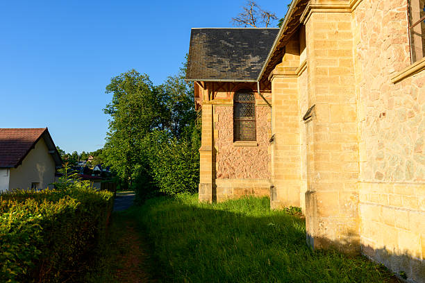 Old stone church facade illuminated by warm evening light, with lush green grass and leafy trees nearby in Saint-Honore-les-Bains.