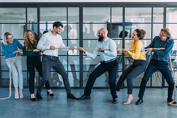 istock Playful colleagues having fun while playing tug-of-war in the office. 2254867940