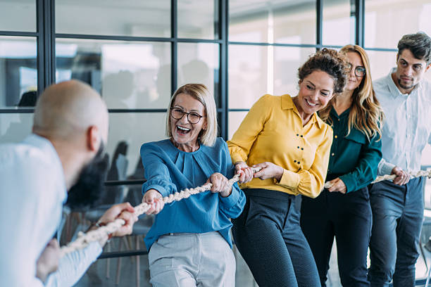 istock Playful colleagues having fun while playing tug-of-war in the office. 2254867941