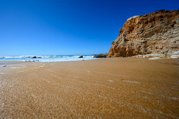 Golden sand meets the turquoise sea at a secluded beach. Waves gently roll in, creating a peaceful scene beneath a clear blue sky, perfect for relaxation.